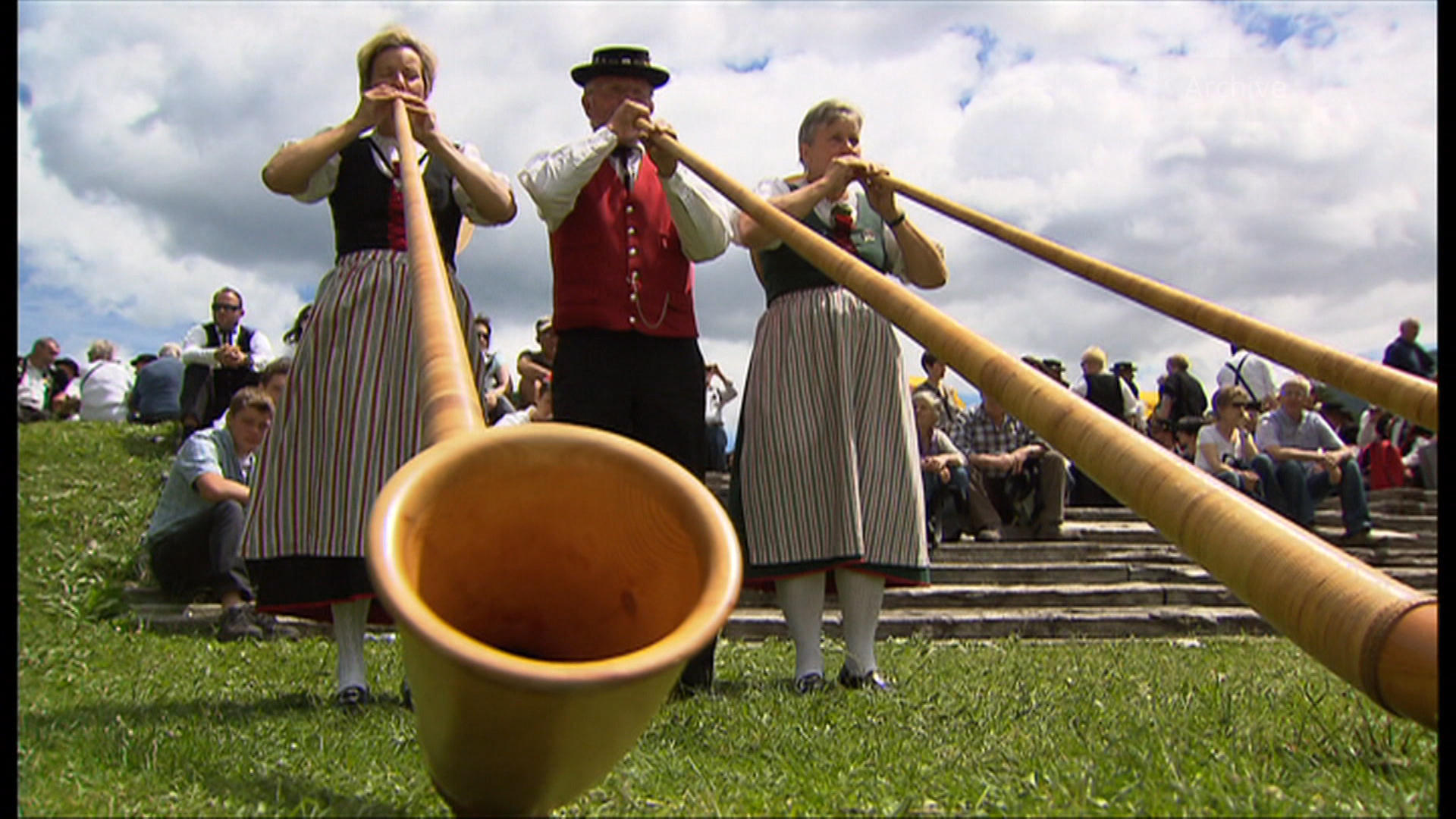 Two women and one man playing the alphorn.