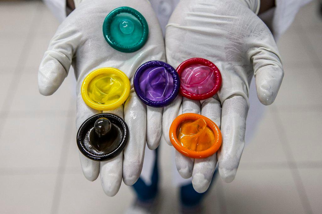 Mãos segurando vários preservativos coloridos