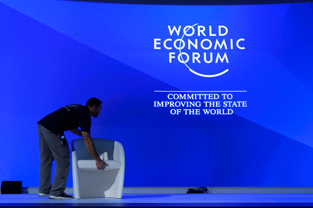 A person places a chair on a stage lit up by the World Economic Forum logo