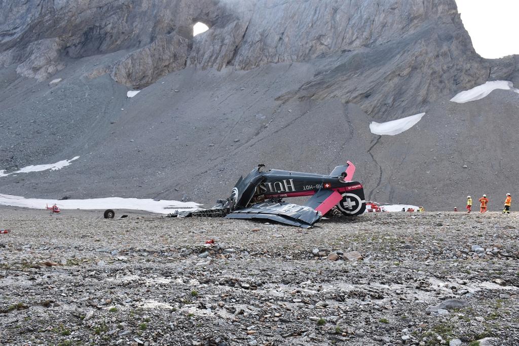 Ein schwarzes Flugzeugwrack liegt auf einer steinigen Ebene in den Bergen.