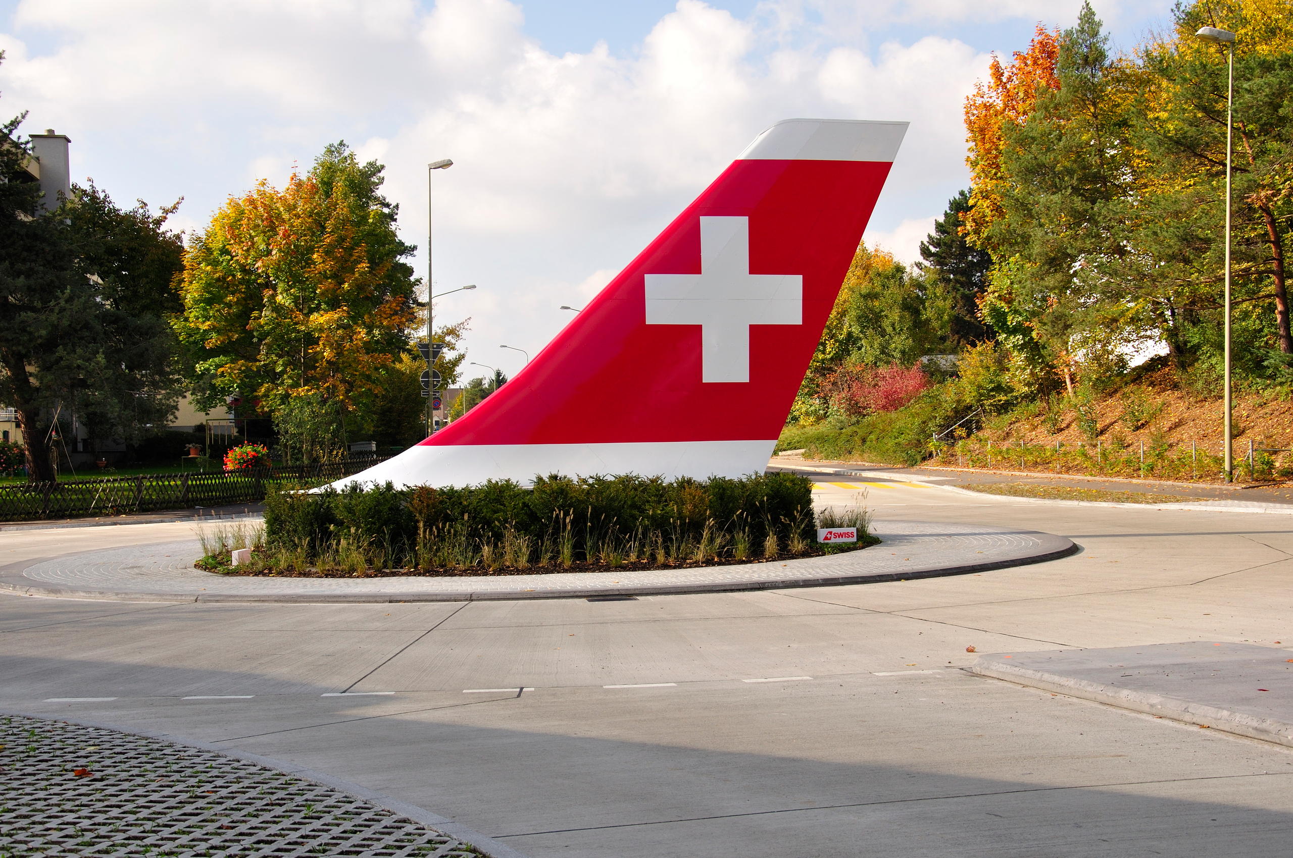 Tail wing of a Swissair aeroplane situated in bushes on a roundabout