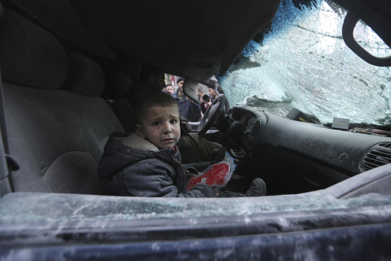 A boy cries, sitting in a destroyed car