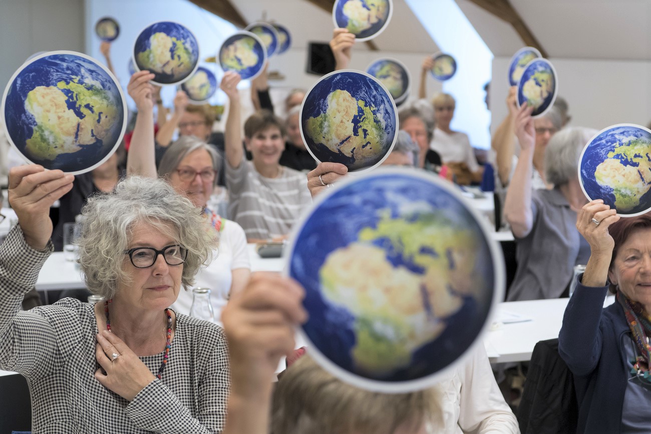 Ältere Frauen heben eine runde Karte hoch, auf welcher der Planet Erde abgebildet ist