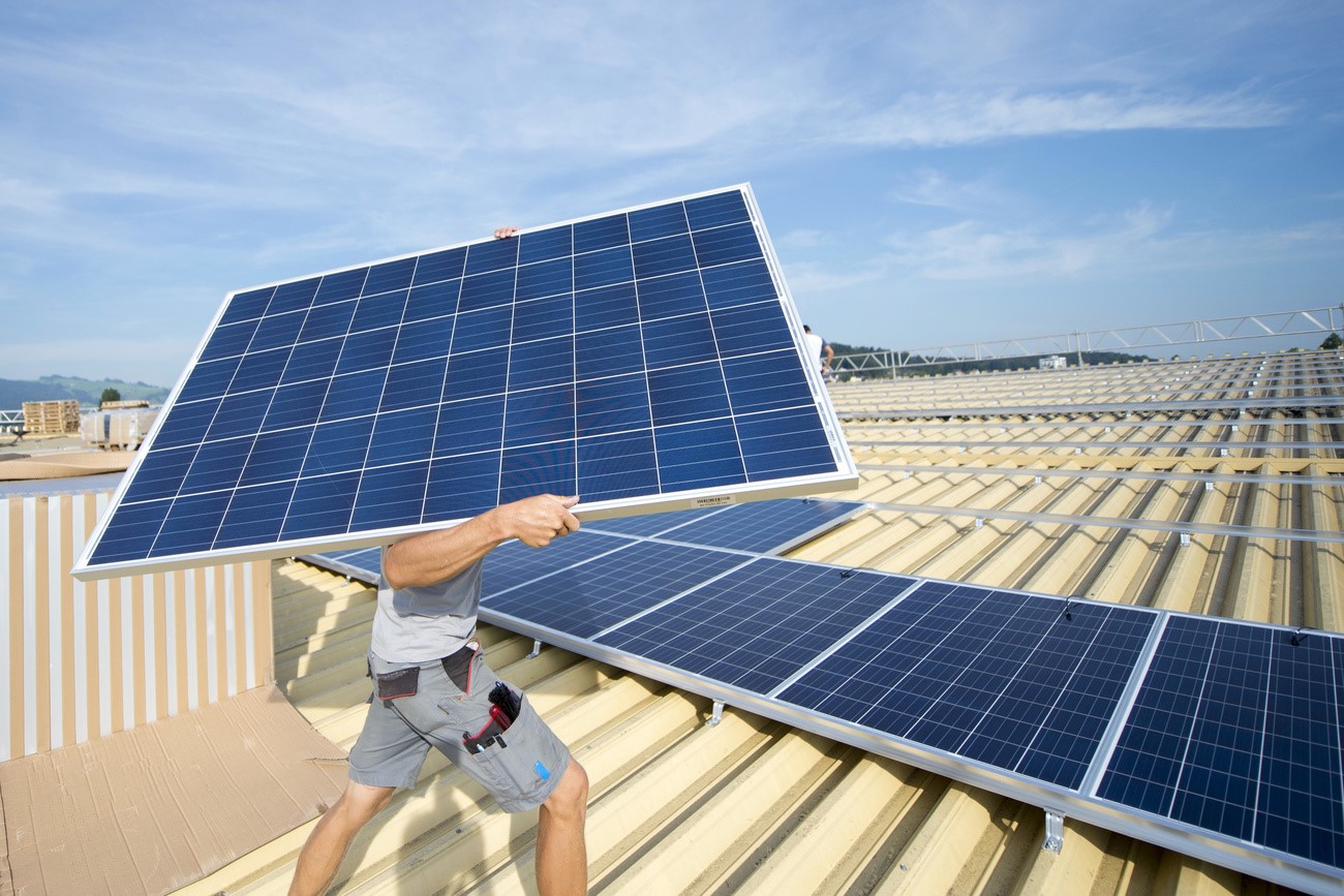 Un hombre transporta un panel solar en un tejado