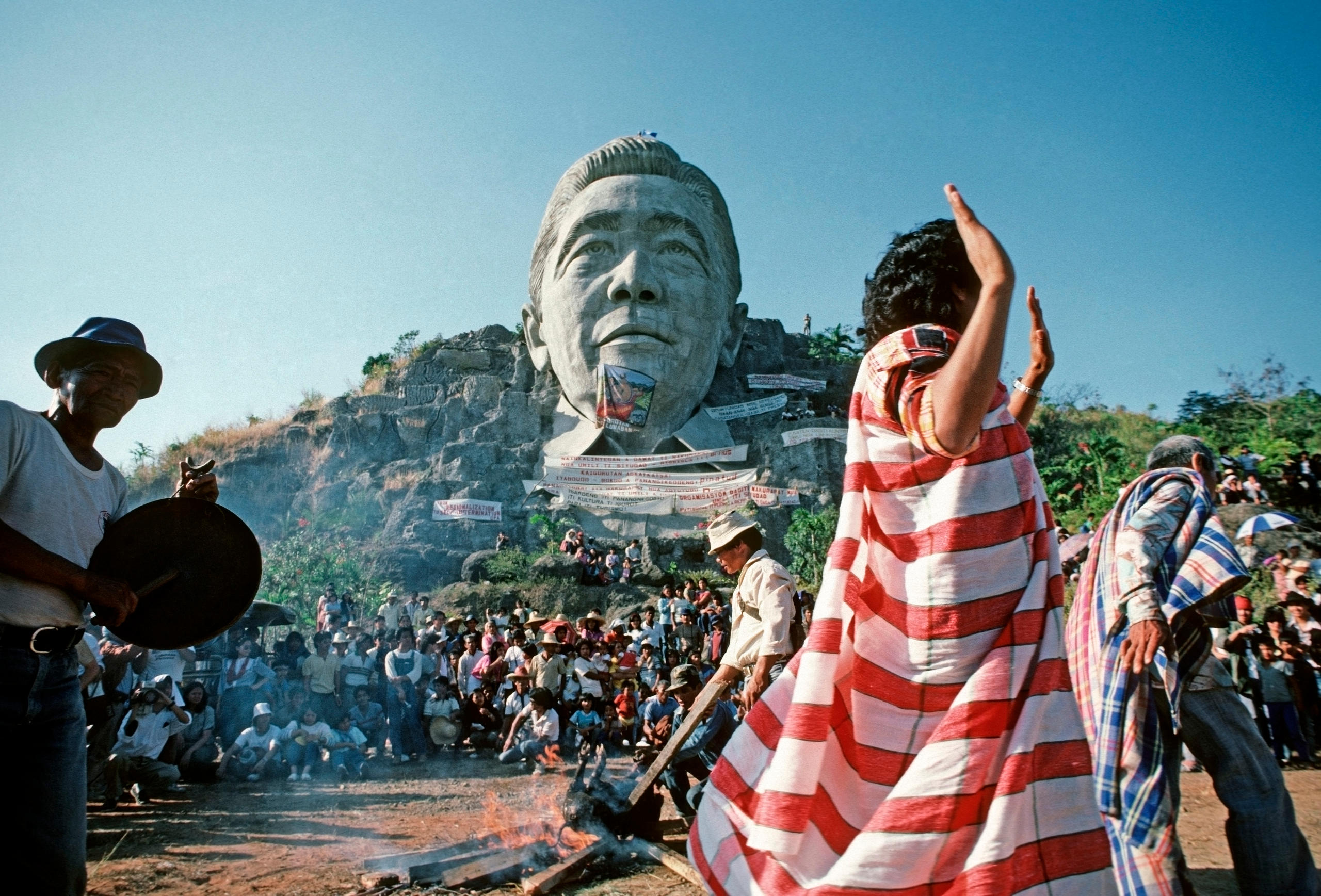 Campesinos filipinos bailando frente al enorme monumento a Ferdinand Marcos