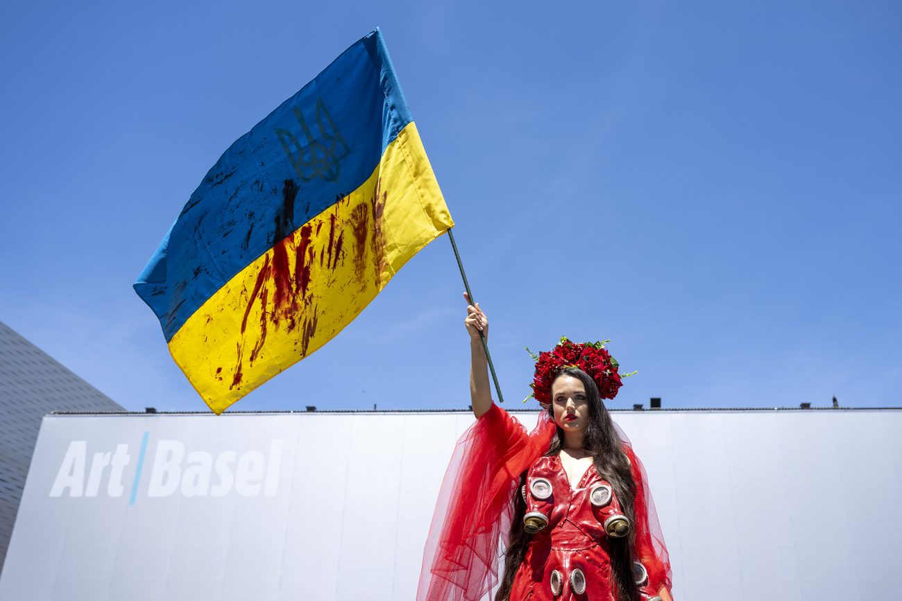 Ukrainian artist raises an Ukrainian flag with the Art Basel building in the background