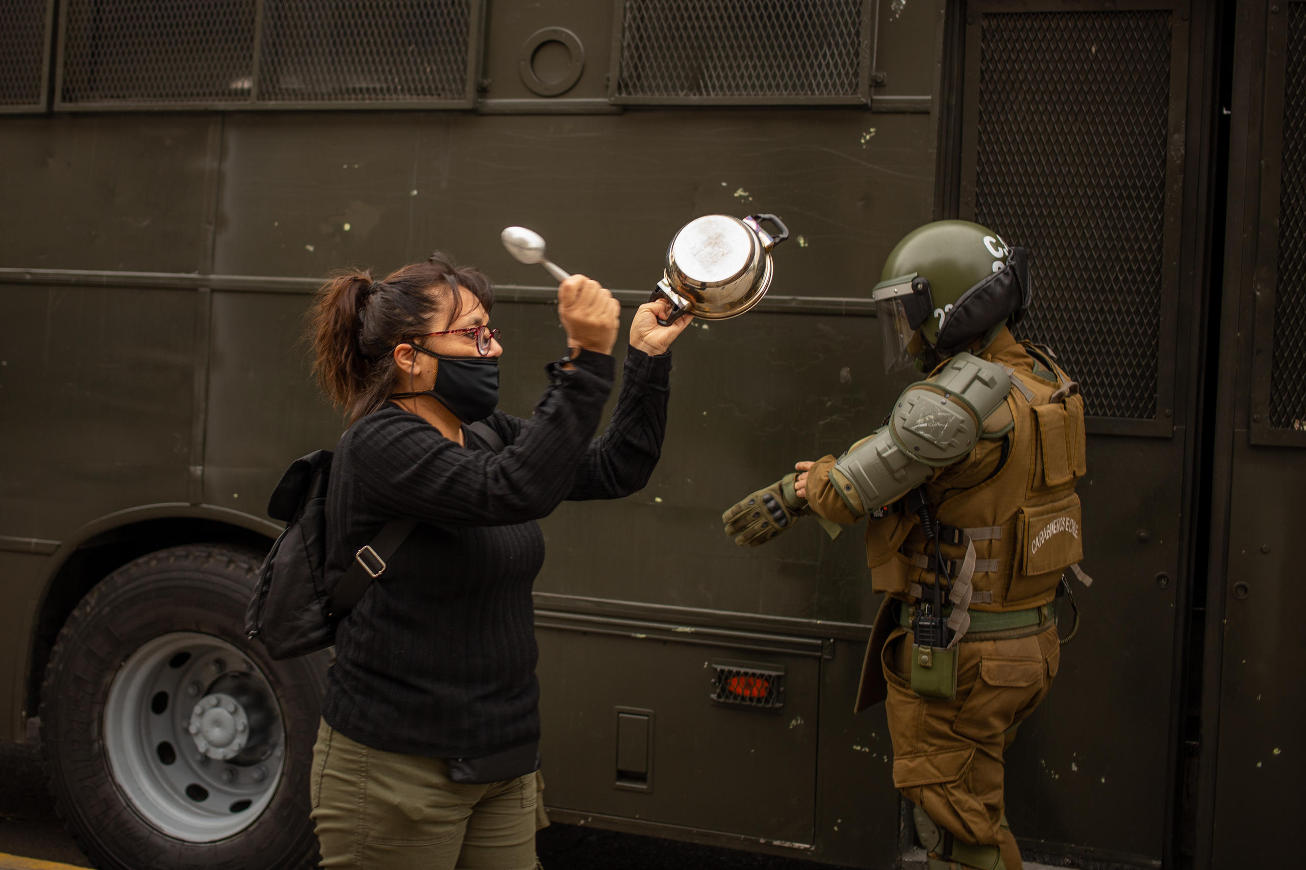 Femme tapant sur une casserole devant un policier casqué
