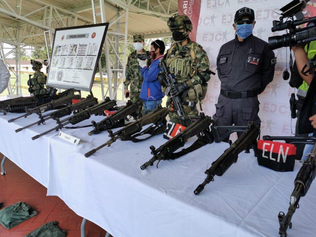 Uma mesa repleta de armas e policiais por trás