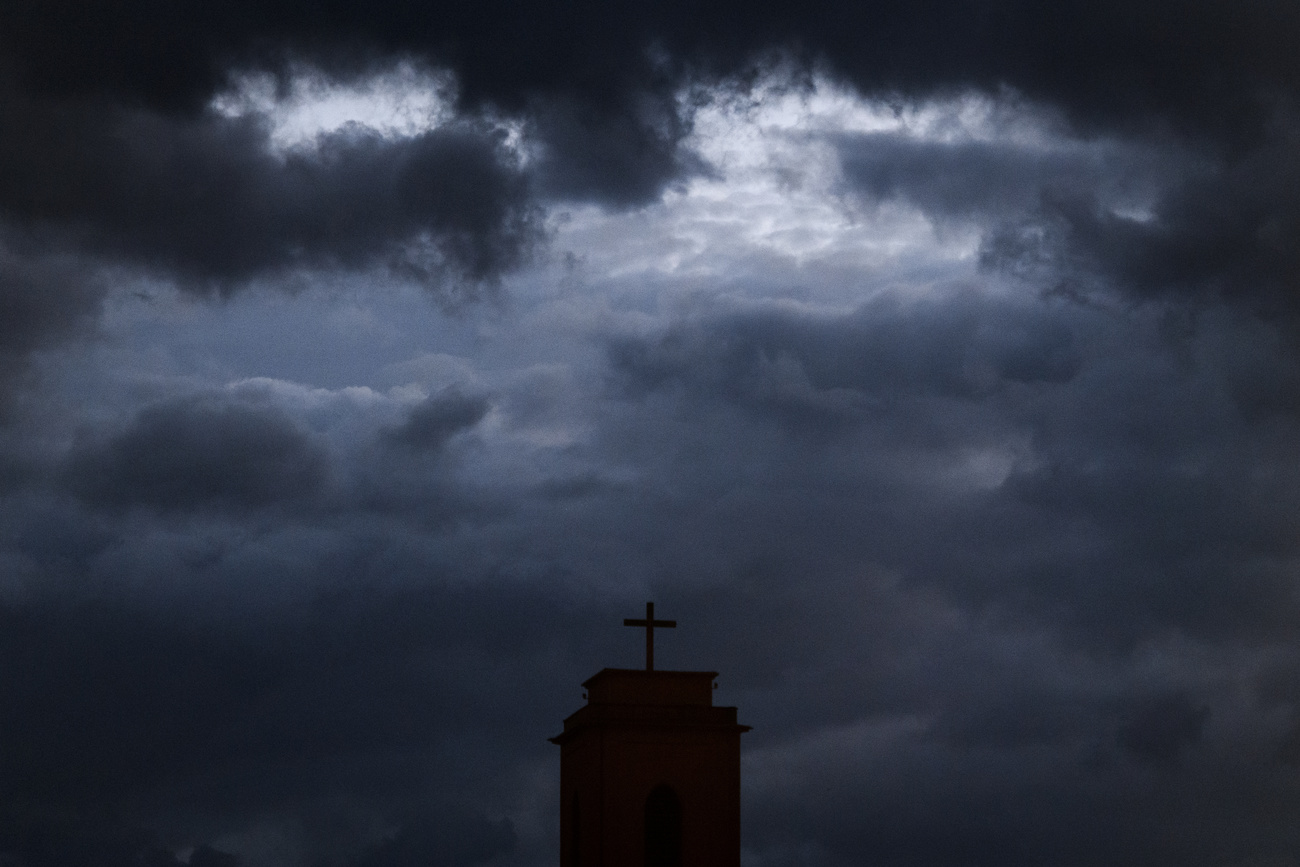 Sotto un cielo plumbeo, si vede una croce in cima a un campanile.