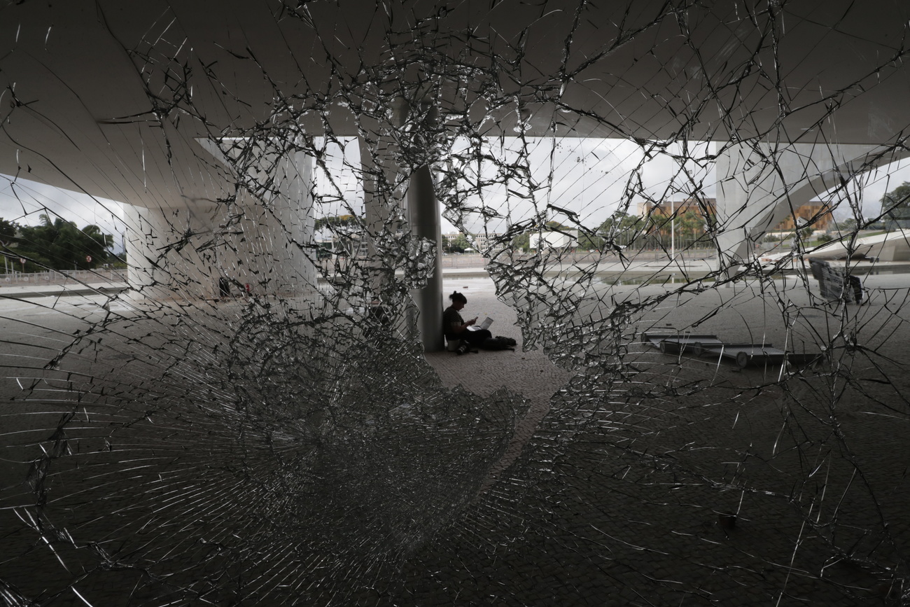 Person sitzt hinter dem zerbrochenen Fenster des brasilianischen Kongressgebäudes