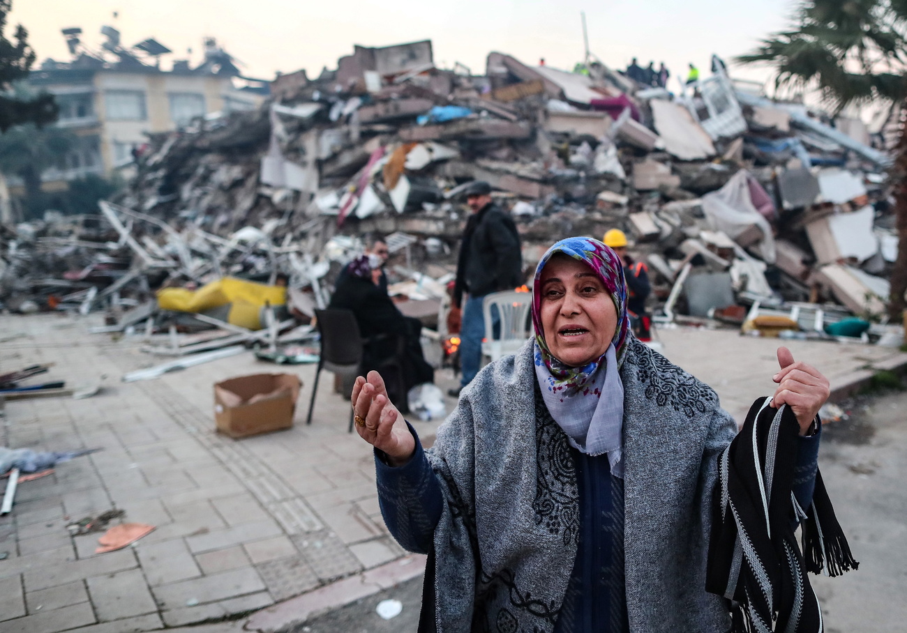 woman reacts in front of collapsed buildings