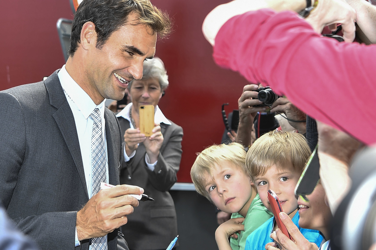 Roger Federer in Anzug und Krawatte gibt Kindern vergnügt Autogramme.