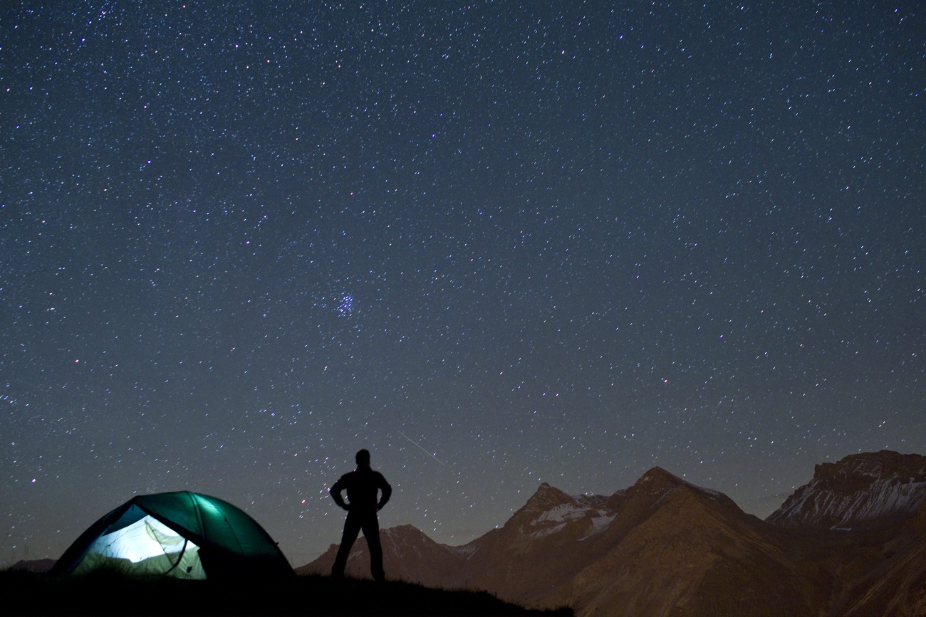 una persona accanto a una tenda ammira un cielo notturno con molte stelle