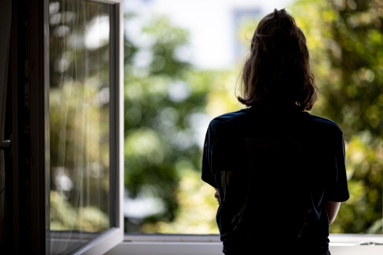 Una ragazza ripresa dalle spalle davanti a una finestra aperta.