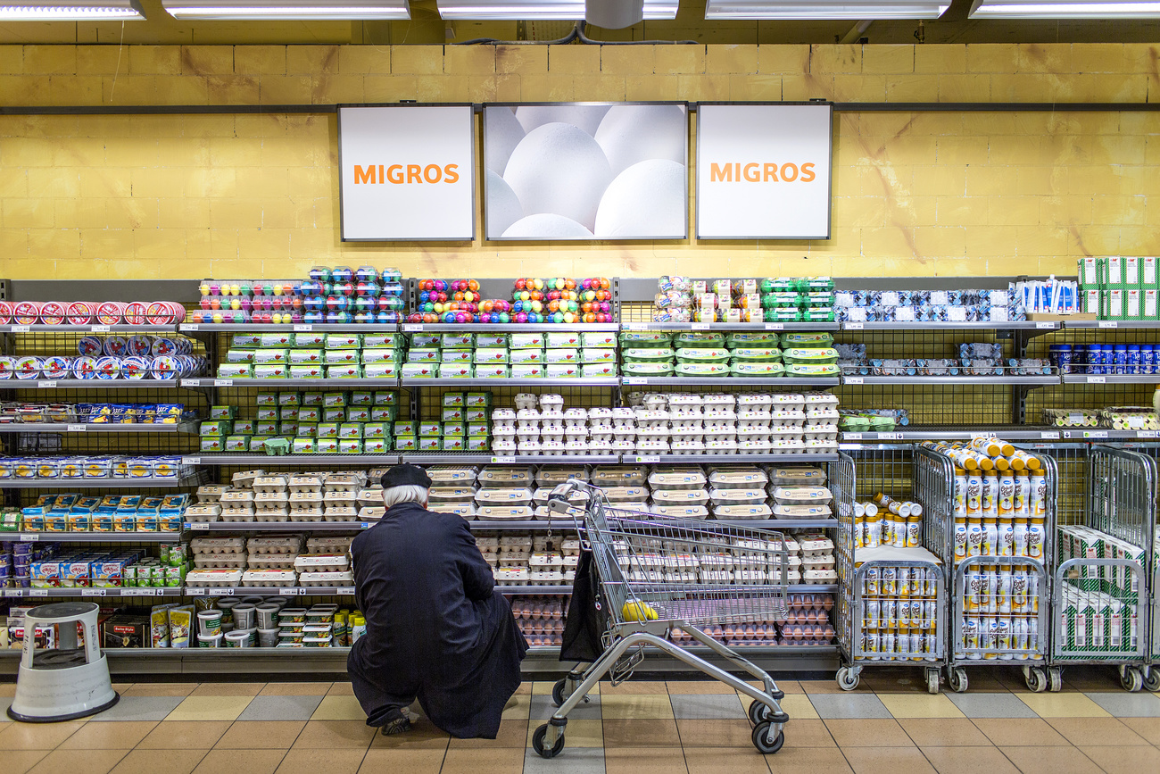 Un uomo inginocchiato guarda attentamente i prezzi dei prodotti in un supermercato.
