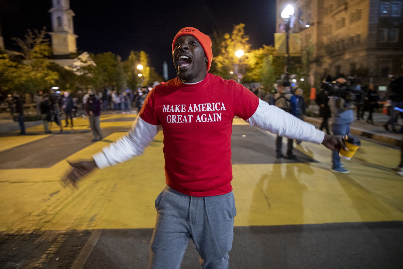 رجل يرتدي قميصًا يحمل عبارة لنجعل أمريكا عظيمة مرة أخرى يصرخ في اتّجاه الكاميرا.