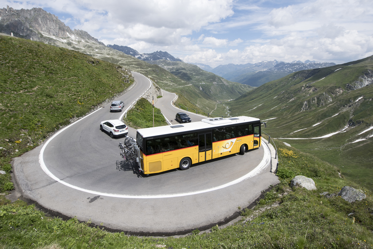 A yellow postauto bus in the rural swiss mountains taking a very sharp curve