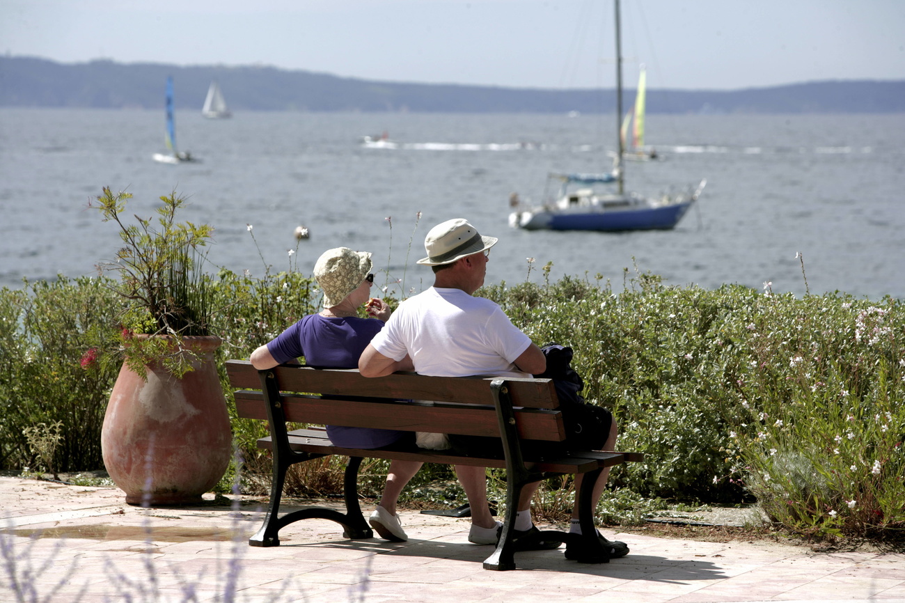 two elderly people sitting on a bench in front of the sea