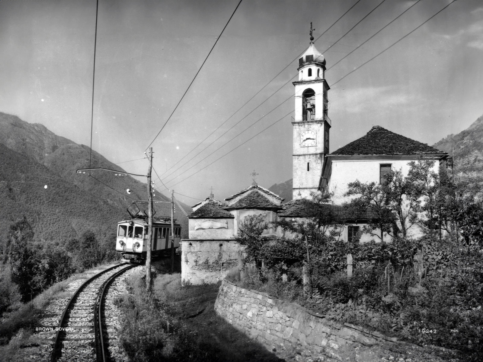 Foto em preto e branco mostrando um trem e uma torrre de igreja