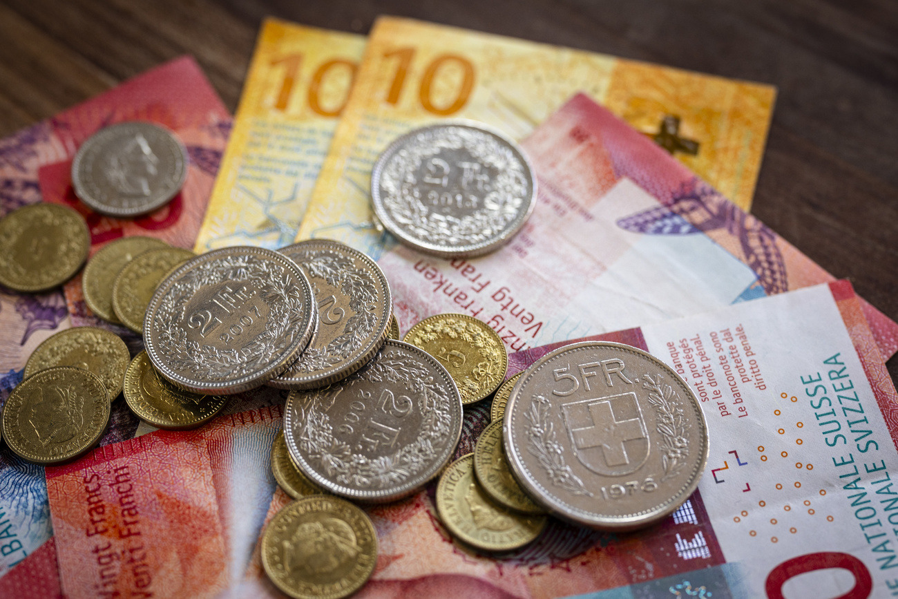 Gold and silver Swiss coins piled on top of yellow 10 franc notes and red 20 franc notes