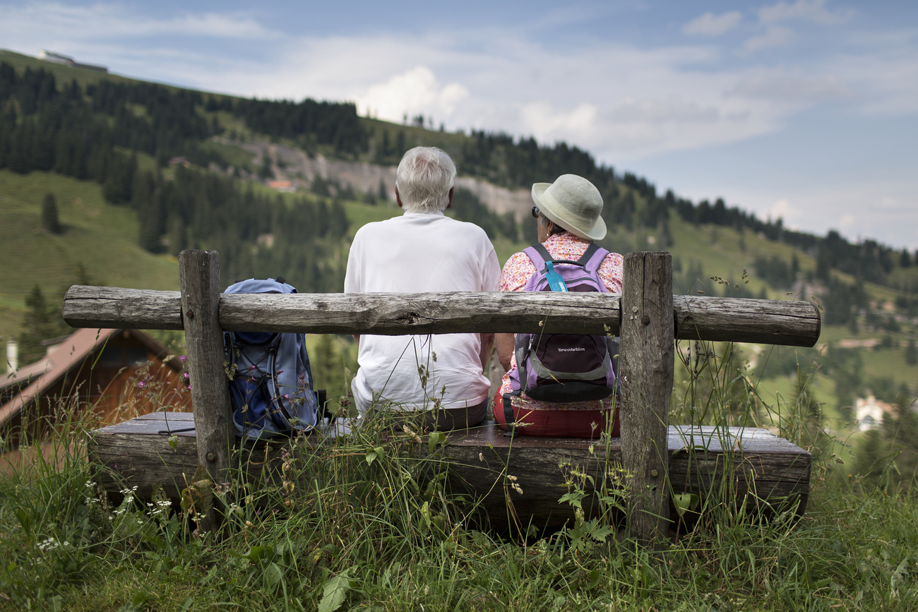 Un'anziana coppia seduta su una panchina in montagna.