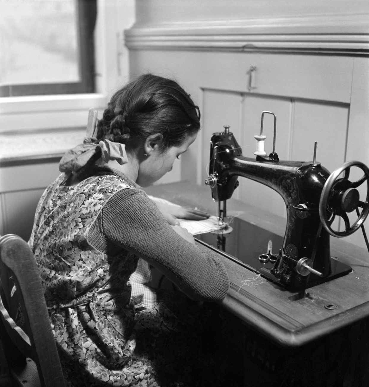 Schwarz-Weiss-Foto: Eine Junge Frau arbeitet an einer Nähmaschine