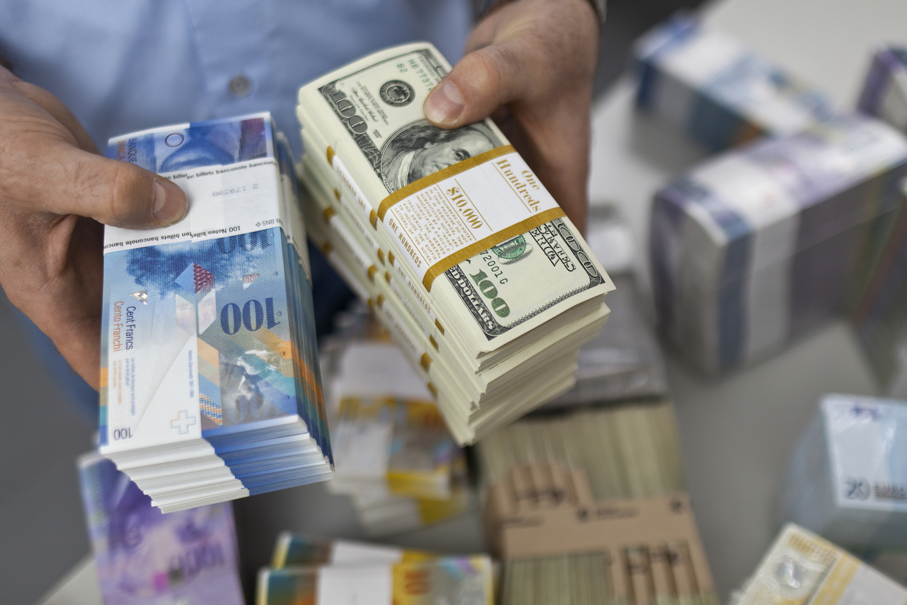A person holds bundles of blue 100CHF notes and green $100 bills