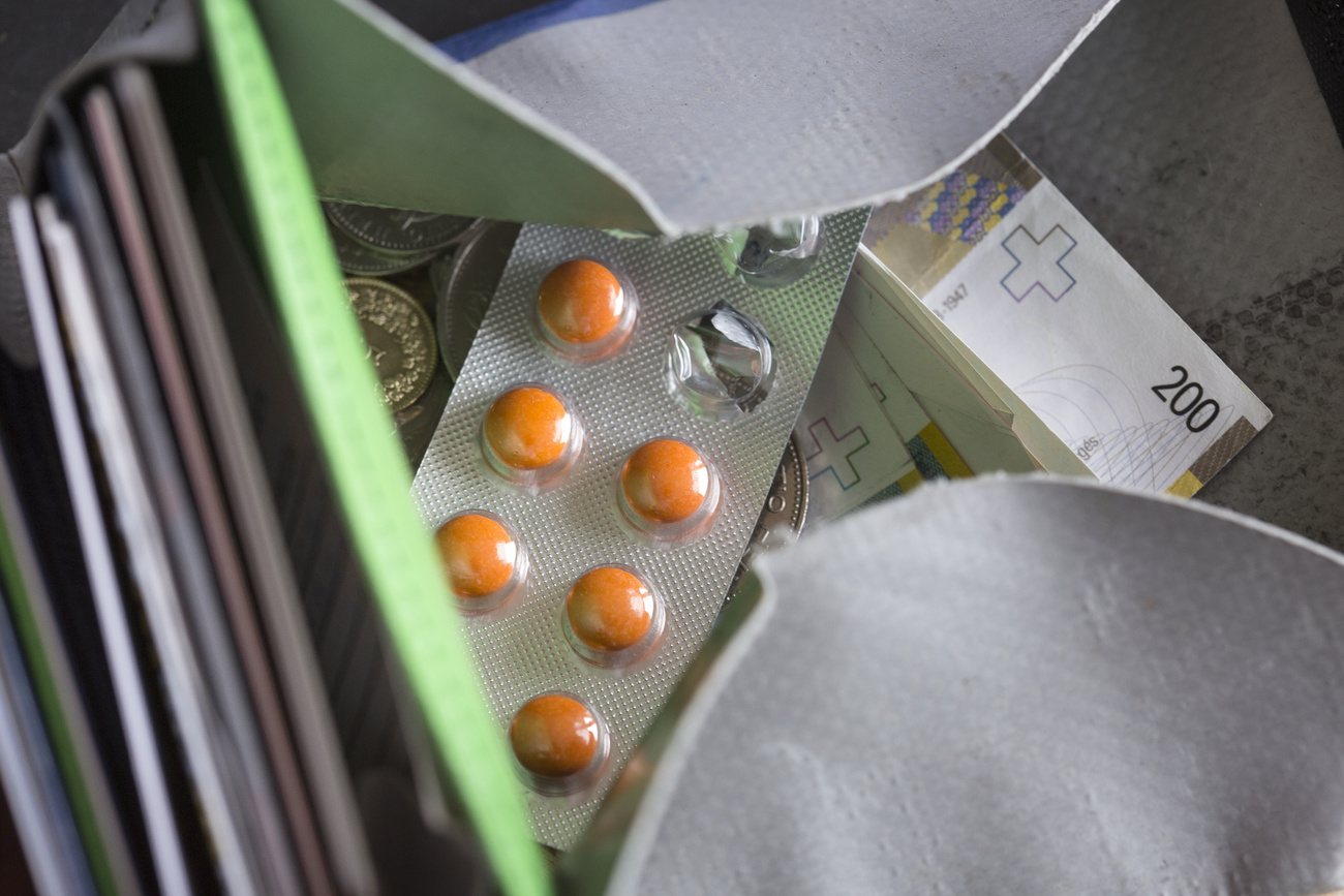 Inside a wallet, a foil pill packet with individual orange pills, three of which are empty, as well as Swiss coins and a CHF200 note.
