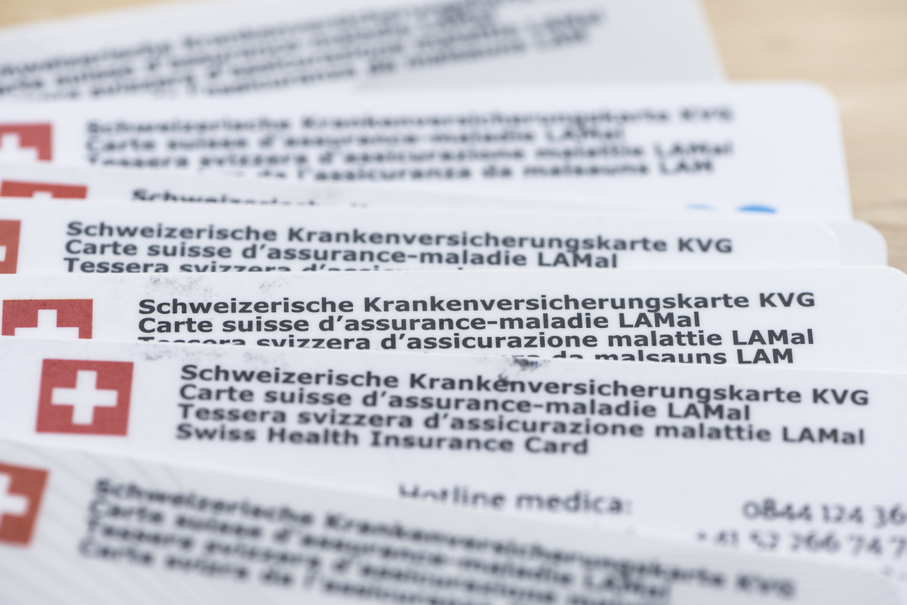 A pile of white Swiss health insurance cards, with the Swiss flag (a red square with a white plug) visible in the left hand corners
