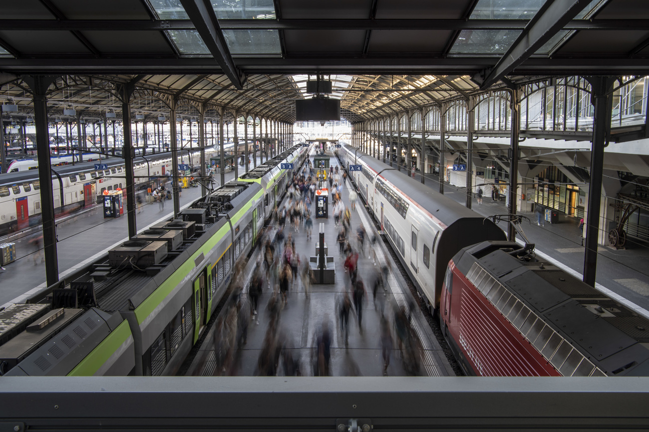 A view of several trains sitting on tracks and a large number of commuters at Bahnhof Luzern.
