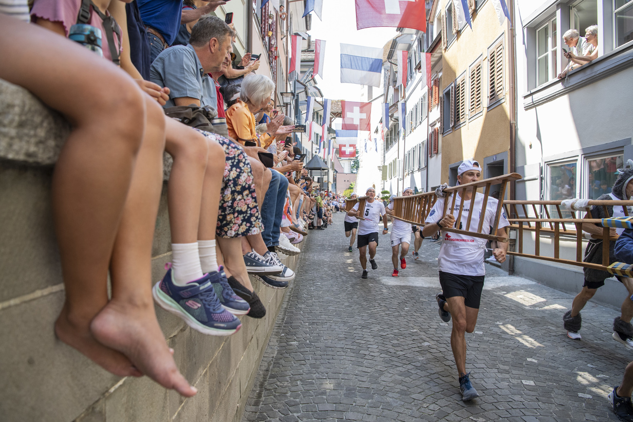 Männer mit Leitern rennen vor Zuschauenden durch die Zuger Altstadt.