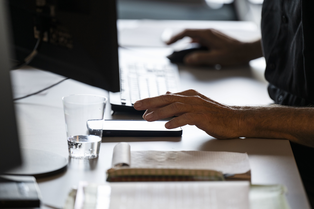 A person is shown seated at a desk, using a computer and a mobile phone.