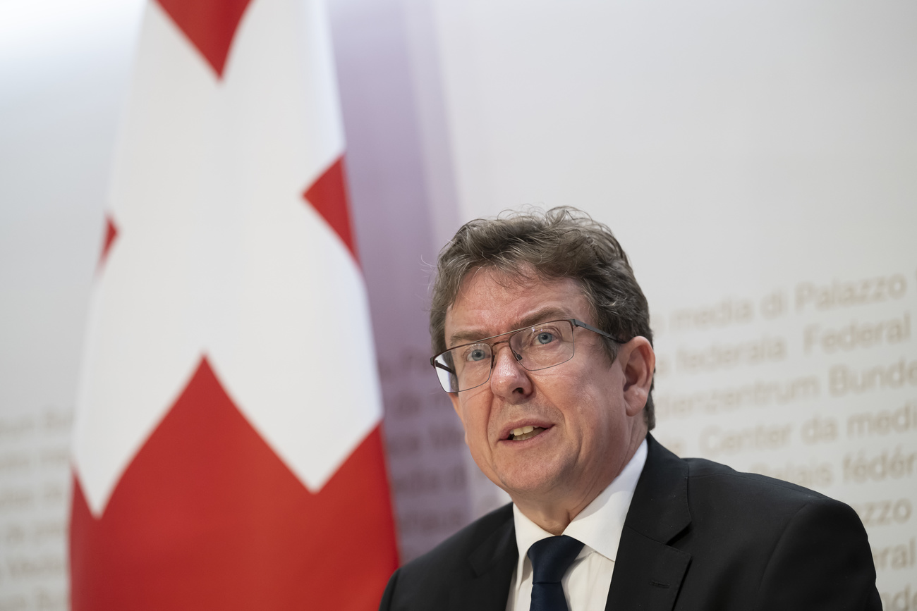communication minister Albert Rösti speaks at a press conference with a Swiss flag behind him.