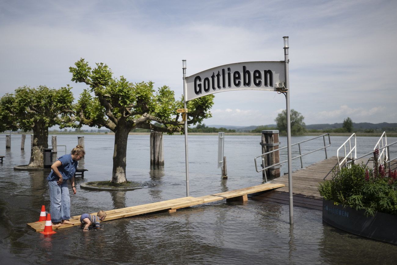 a mother and small child wade through water near a sign which reads "Gottlieben" at a pier.
