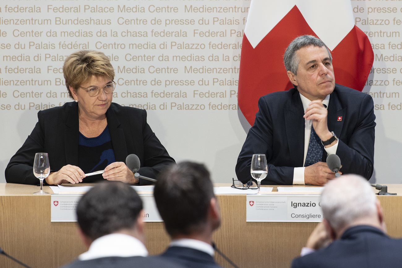 Swiss president Viola Amherd and foreign minister Ignasio Cassis sit behind a desk listening to a question while reporters in the foreground listen at a press conference
