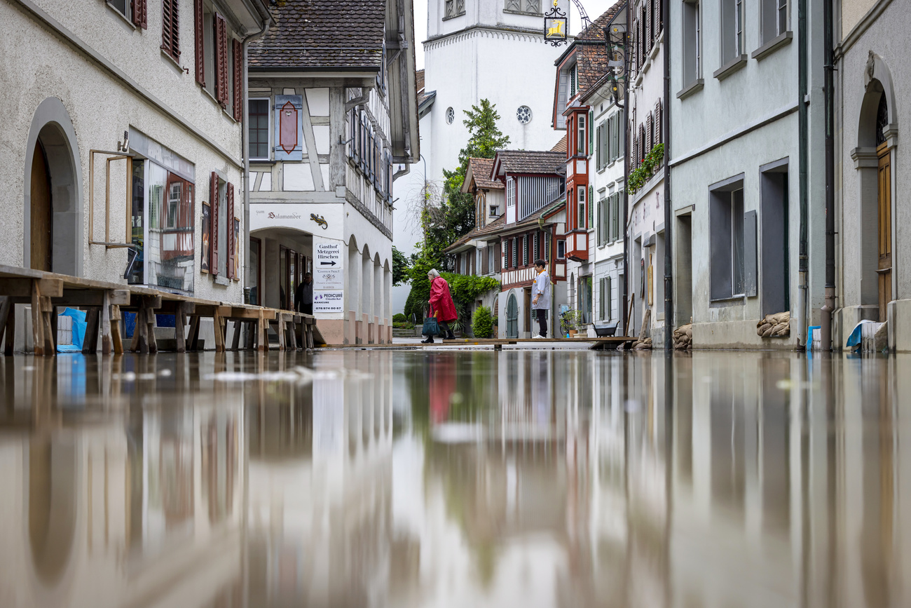 Two women cross a temporary footbridge as the Lake Untersee, the western part of Lake Bodensee overflows its banks, in Berlingen, Switzerland, on Tuesday, June 11, 2024. On Tuesday, the federal government declared the highest danger level for the western part of Lake Bodensee. In several places, lakeside promenades, parking lots and garden restaurants are under water. Mobile dyke systems and sandbags are being used to try and hold back the water from the lake. (KEYSTONE/Michael Buholzer)