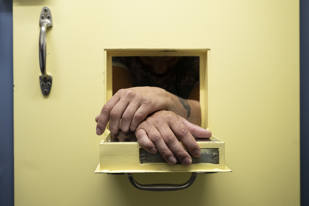 a prisoner's hands are seen resting on a small open access door in his prison cell door.