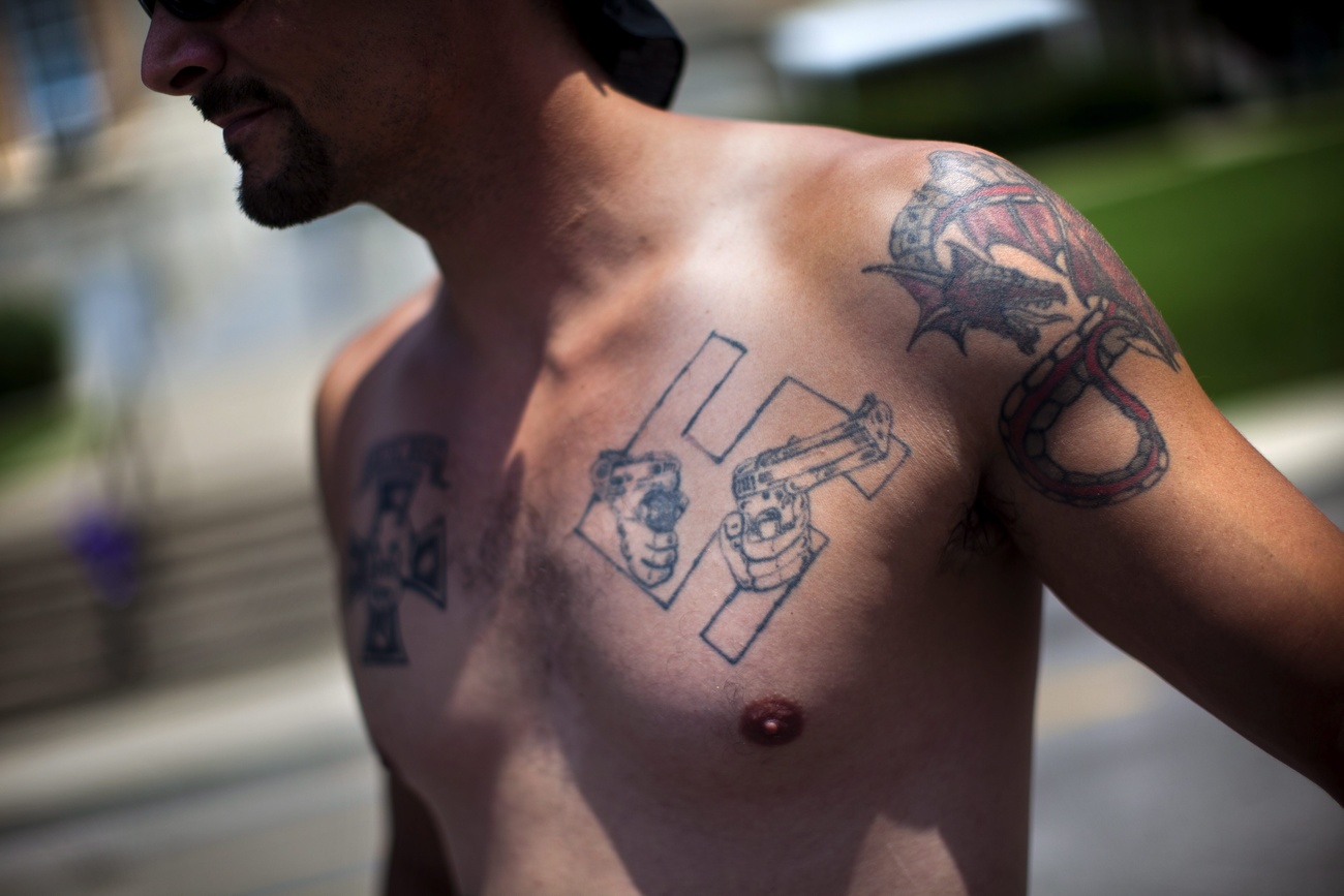 uomo a petto nudo con tatuaggio di svastica su pettorale sinistro