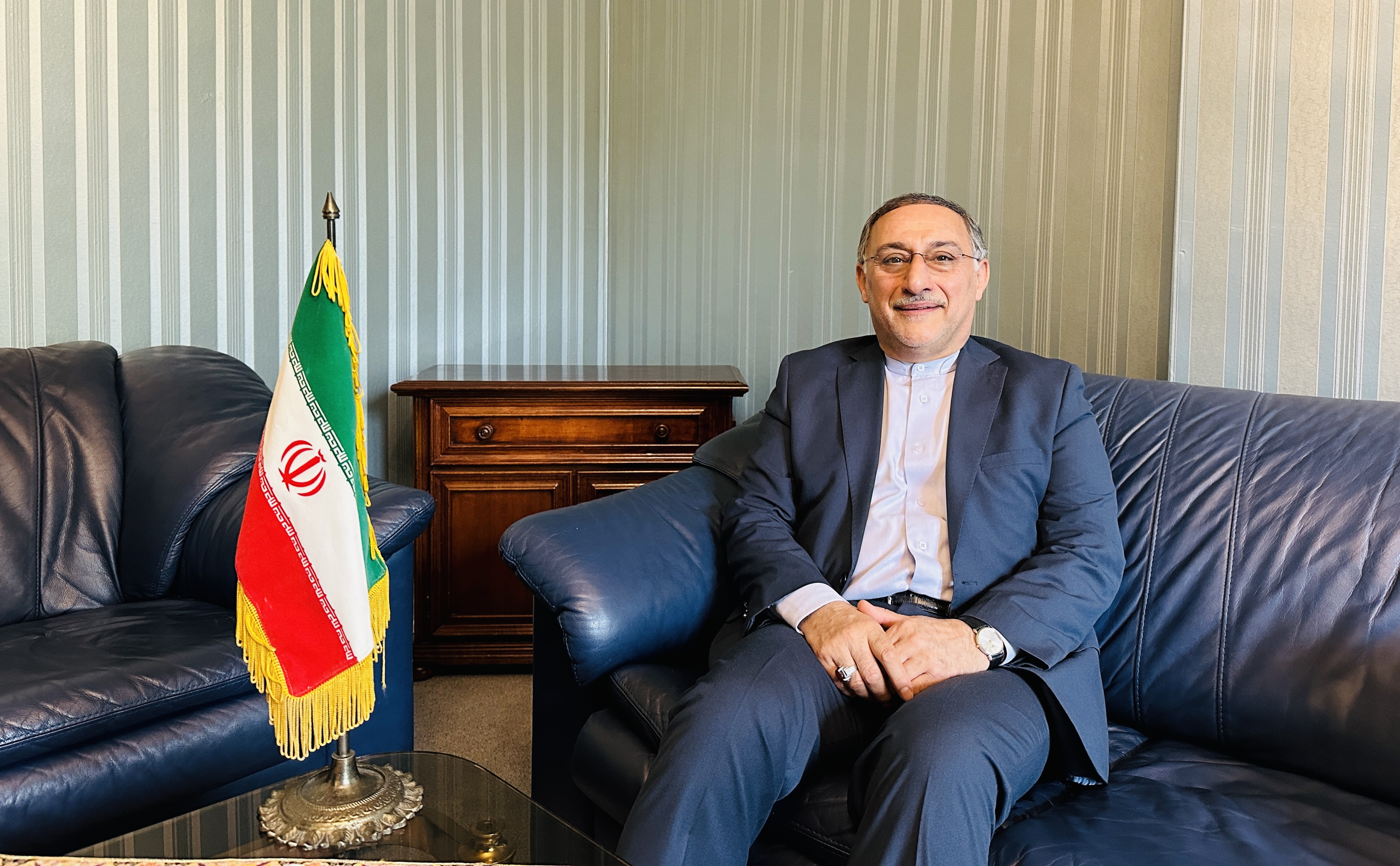 Mahmoud Barimani auf einem Sofa neben einer Iran-Flagge.