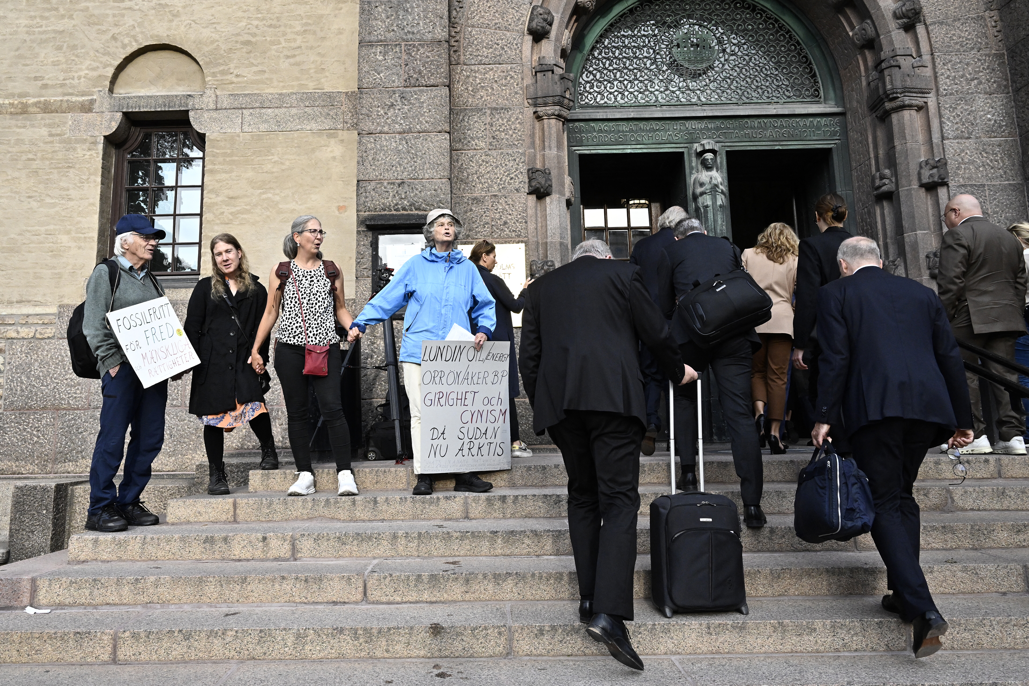 Menschen betreten das Gerichtsgebäude und eine Gruppe demonstriert