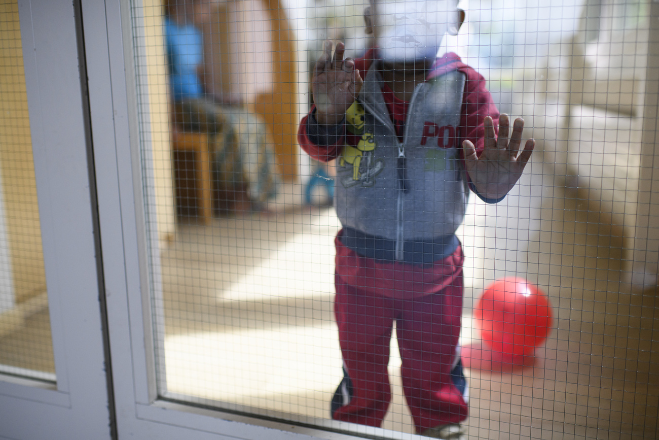 bambino di meno di due anni in piedi dietro a una porta a vetri aalla quale si appoggia