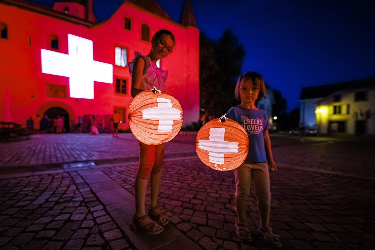 two small children hold a lit up balloon of swiss flags with a swiss flag projected in the bacl