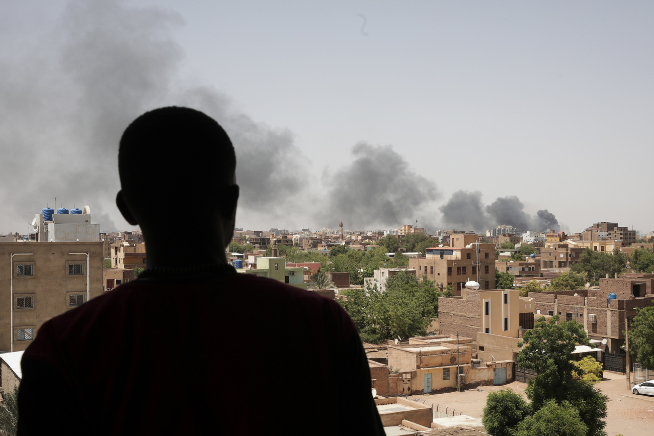 Photo of a man from the back overlooking a city in Sudan with smoke from fighting.
