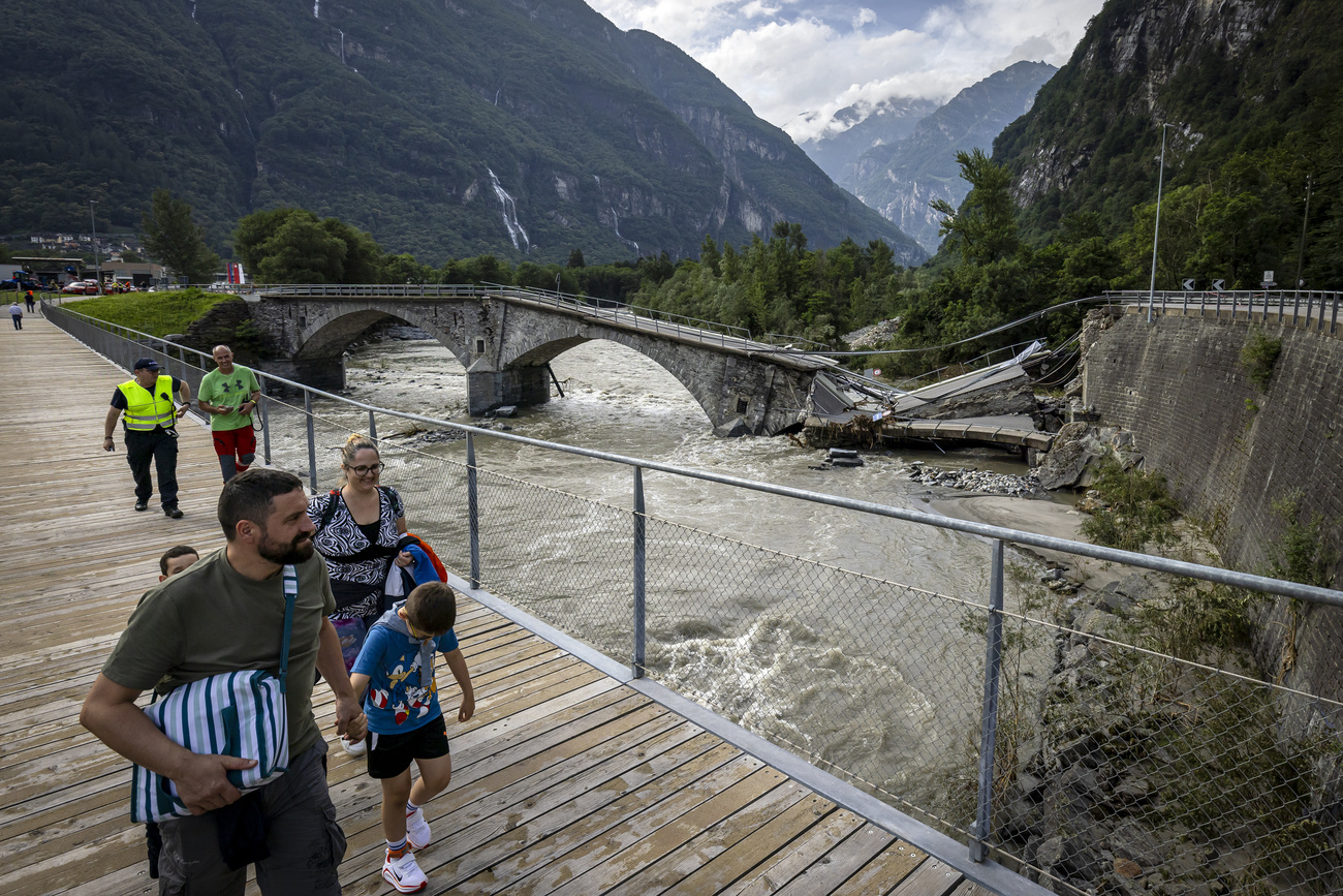 Pedestrians leave Cevio via a pedestrian bridge next to the collapsed Visletto bridge between Visletto and Cevio, in the Maggia Valley, southern Switzerland on Sunday June 30, 2024. The storm in the night from Saturday to Sunday destroyed various traffic routes. On Sunday morning, the bodies of two women were recovered in Val Bavona near a landslide. A third body was later found in the same area. A fourth missing person was still being searched for in the Lavizzara Valley on Sunday. (KEYSTONE/Michael Buholzer).
