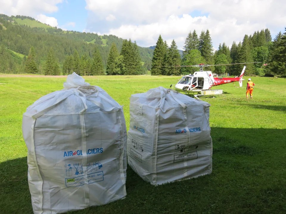 two white sacks on a green frield with a red and white helicopter in the background