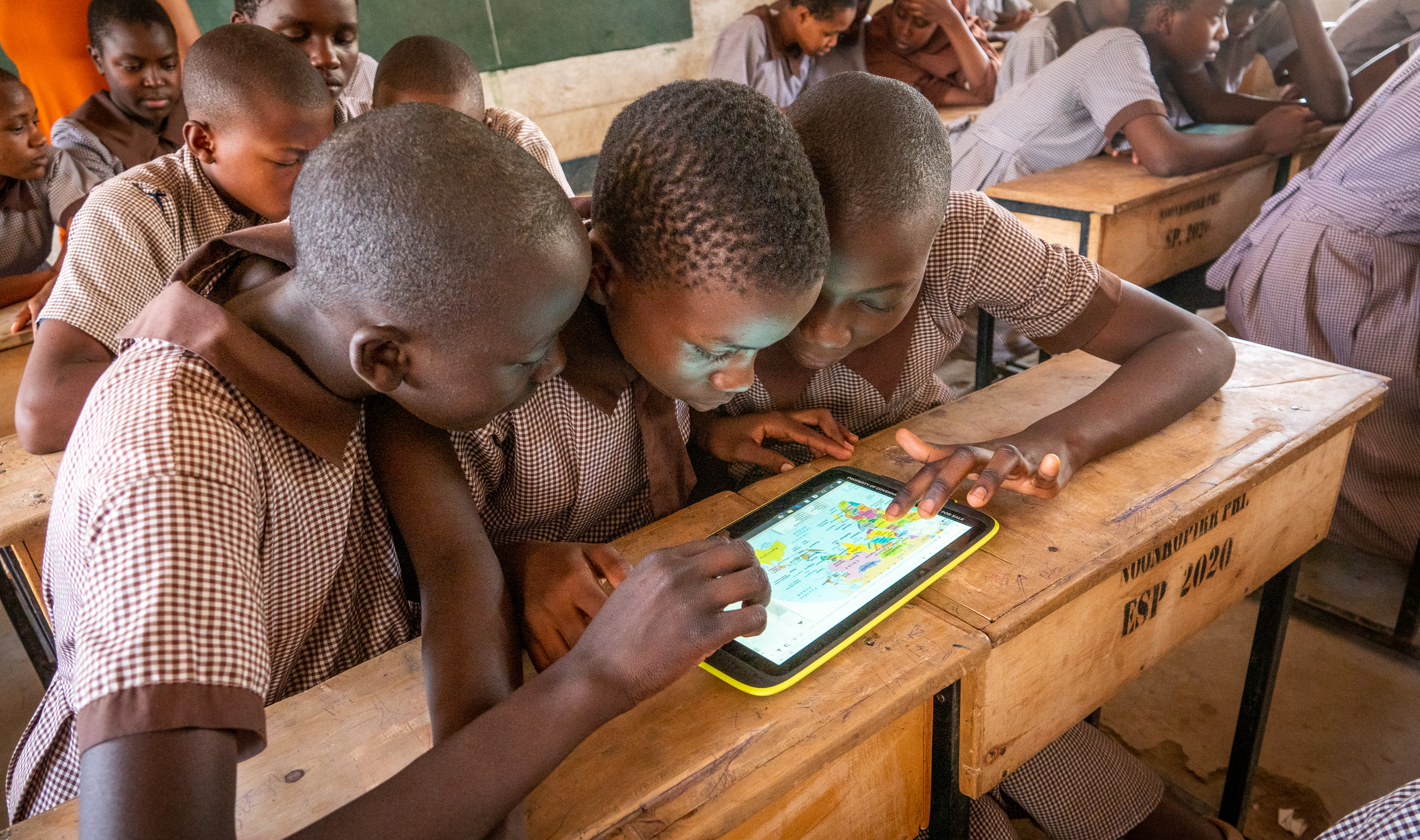 Three Kenyan schools in a girl are looking at the image of a world map on an iPad.