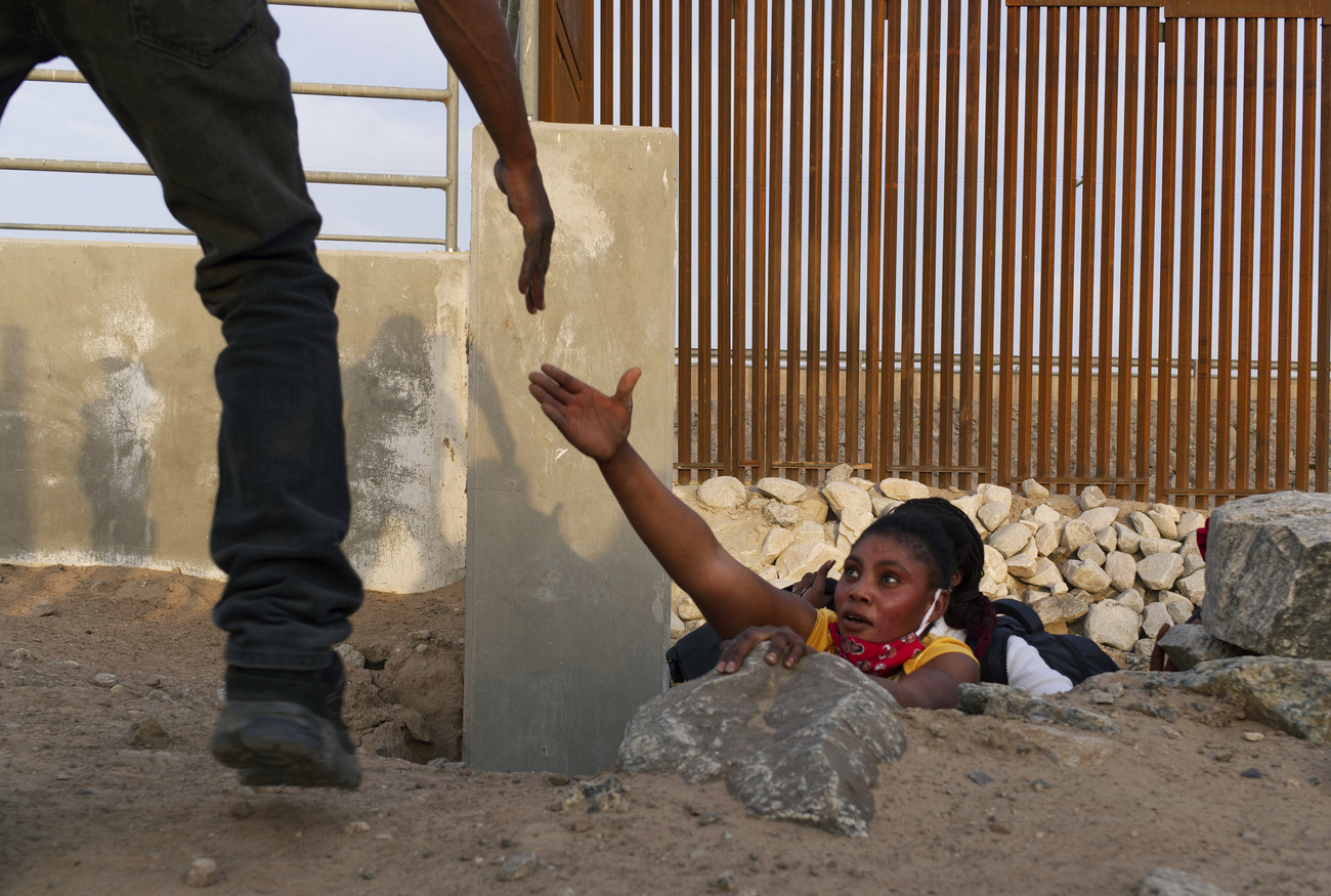 Un miembro de una familia de migrantes haitianos pide ayuda mientras emerge de un canal rocoso adyacente a una brecha en el muro fronterizo de Estados Unidos en Yuma, Arizona.