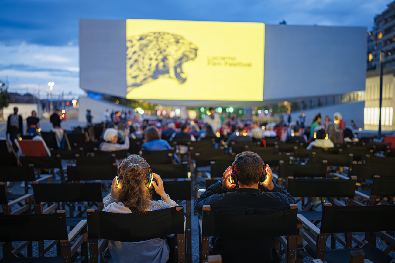 people watch a yellow screen with a black and yellow leopard. People watching are wearing headphones that are glowing orange.