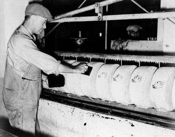 Foto in bianco e nero, operaio in un caseificio timbra il formaggio con un timbro del Wisconsin.