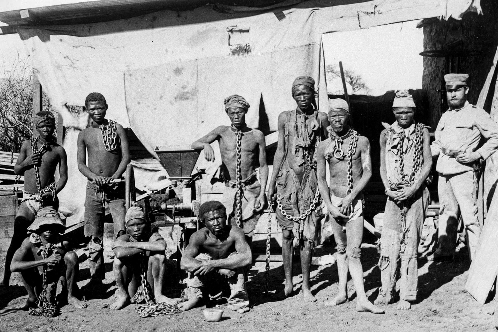 Foto antiga em preto e branco de africanos e militares europeus.